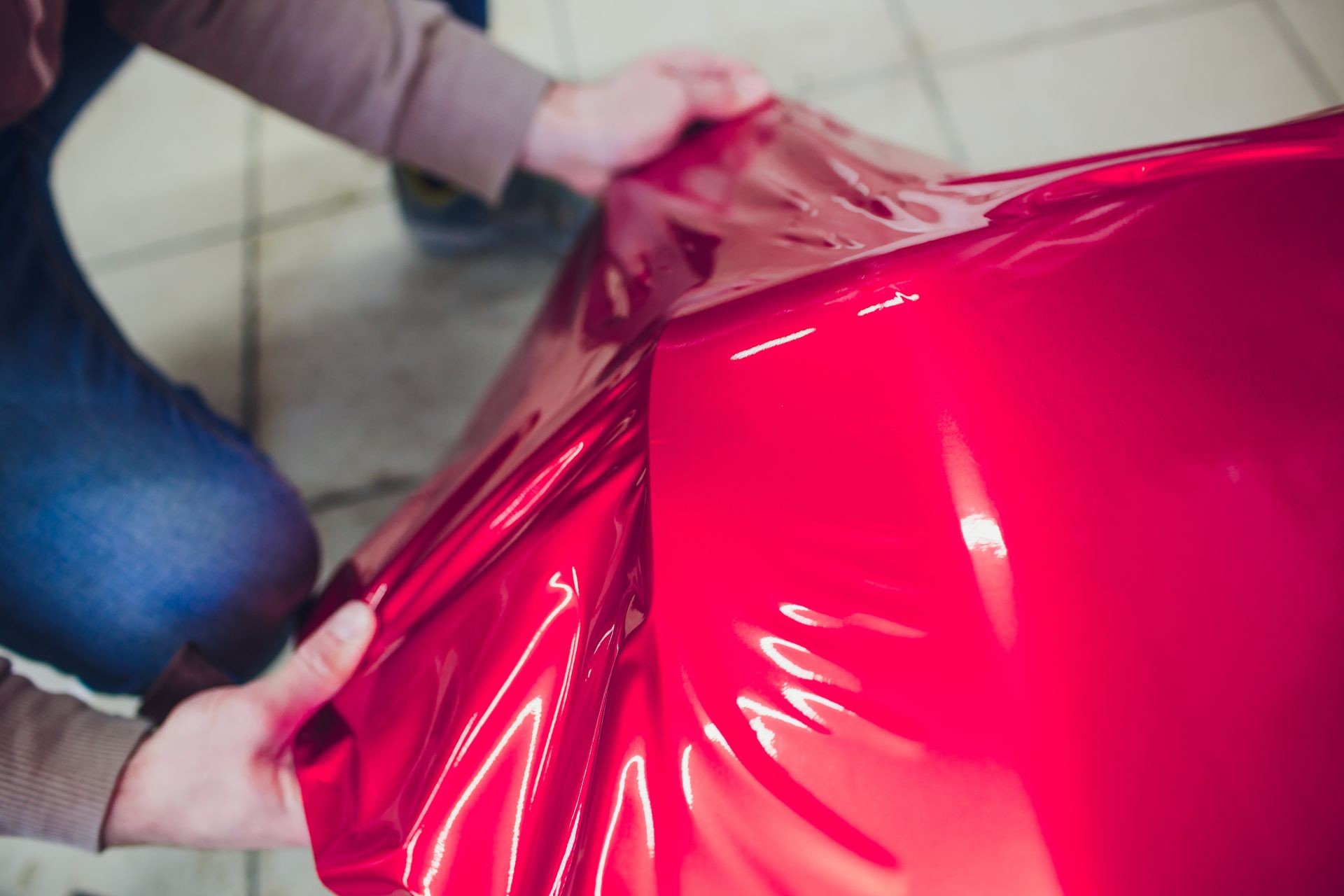 Car wrapping specialist putting vinyl foil or film on car wrapping protective film yacht, boat, ship, car, mobile home. pink red film hand pulls Car wrapping specialist putting vinyl foil or film on car wrapping protective film yacht, boat, ship, car, mobile home. pink red film hand pulls